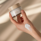 Hand holding a jar of 'Rice Cream' with a swatch on skin against a beige background