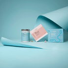 Advanced Nutrition Programme Radiant Skin Biome Duo box, Skin Omegas+ tin and Skin Youth Biome box arranged on curled pale blue paper, with capsules scattered in front.